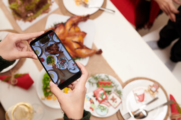Naklejka na ściany i meble Hands of person taking photo of Christmas dinner to upload on social media