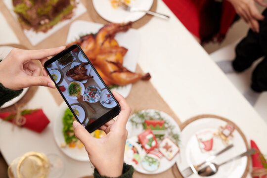 Hands of person taking photo of Christmas dinner to upload on social media