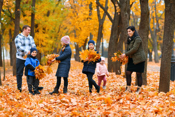 Portrait of a family with children in an autumn city park - happy people walking together, they toss the leaves, beautiful nature with yellow leaves as background.