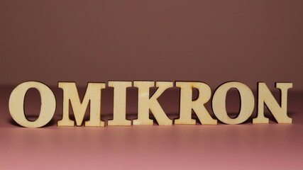 Wooden letetrs make name of new coronavirus variant OMIKRON on pink background, close up