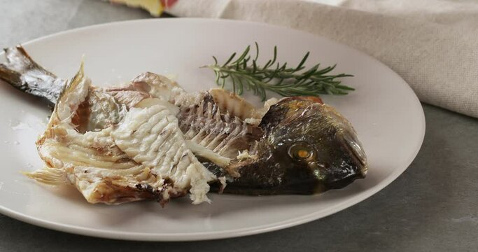Pouring lemon juice on freshly baked gilt-head bream (dorade) fish. Slow motion food footage. 
