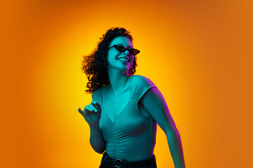 Portrait of young beautiful cheerful girl dancing isolated on yellow brown studio background in neon light.
