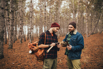 Two millennial man hiking and drinking beer in a forest, laughing and having fun.