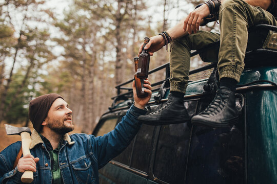 Two Millennial Man Hiking In A Forest, Drinking Beer And Having Fun.