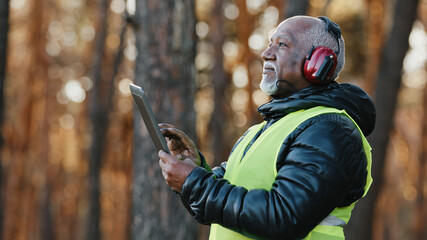 Elderly african american forestry engineer in noiseisolating headphones in forest old mature...