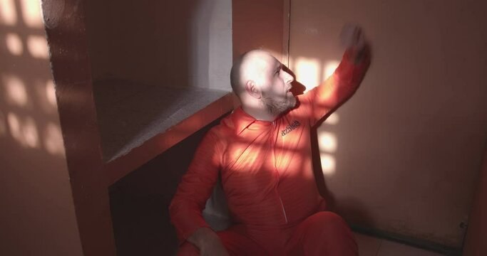 sad prisoner sits on the floor and hits his hand on the prison cell door