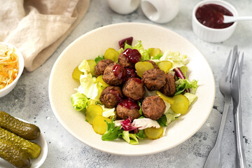 Swedish meatballs with salad, pickled cucumber and lingonberry jam in a bowl. Traditional Scandinavian dish in a ceramic plate on a light gray culinary background closeup