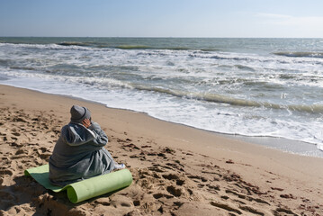 Pretty woman in warm clothes sitting on the cold autumn beach.