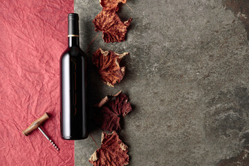 Bottle of red wine with corkscrew and dried vine leaves.