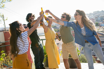 Joyful friends at party on sunny day. People of different nationalities drinking beer at terrace...
