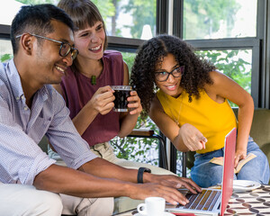 Image of happy young people using laptop while sitting at cafe, young african american woman pointing device, multiethnic group of students in a coffee shop working on laptop