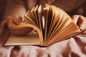 A man, lying on a soft bed, flips through the old pages of a thick interesting book. Self-development at home. Leisure and recreation while reading.