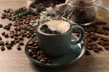 Cup of aromatic hot coffee and beans on wooden table