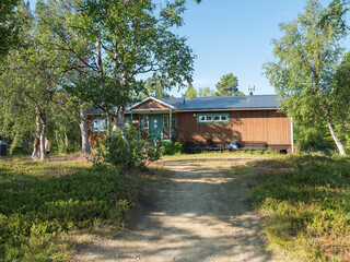 Fototapeta na wymiar Frontal view of one of Saltoluokta Fjallstation STF mountain lodge in birch forest with two backpacks on the bench. Sweden Lapland cabin on famous Kungsleden, Kings hiking trail