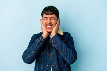 Young mixed race man isolated on blue background covering ears with hands.