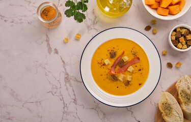 Pumpkin cream soup with croutons and jerky meat chips in a white plate on a light marble background top view. Horizontal orientation, no people