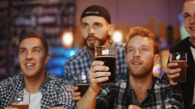 Celebrating victory, knocking glasses. Group of soccer fans together indoors in the pub have fun at weekend time