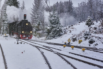 Steam locomotive with smoking and steaming chimney is heading for the snowy switches of the tracks...