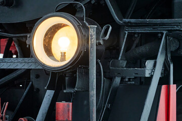 Detail of yellow glowing headlight of old black steam locomotive