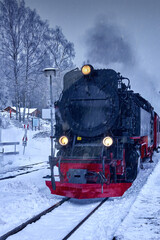 Black steam locomotive with yellow headlights runs over snowy tracks in heavy snowfall