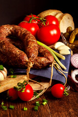 Appetizing smoked homemade sausage with herbs, fresh tomatoes, canned cucumbers, onions, bread and garlic