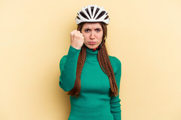 Young caucasian woman wearing a helmet bike isolated on yellow background showing fist to camera, aggressive facial expression.