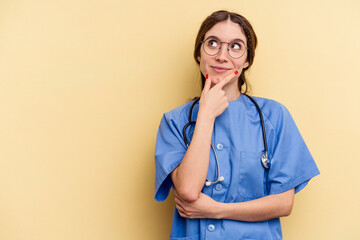 Young nurse caucasian woman isolated on yellow background looking sideways with doubtful and skeptical expression.