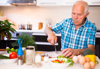 Fototapeta na wymiar elderly man preparing fish at home in the kitchen