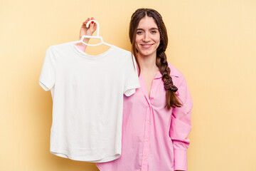 Young caucasian woman holding a hanger isolated on yellow background happy, smiling and cheerful.