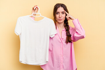 Young caucasian woman holding a hanger isolated on yellow background pointing temple with finger, thinking, focused on a task.