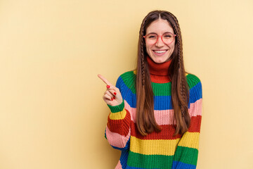 Young caucasian woman isolated on yellow background smiling and pointing aside, showing something at blank space.
