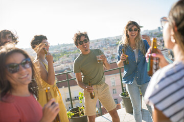 Active friends at party on sunny day. People of different nationalities drinking beer at terrace roof, dancing. Party, friendship concept