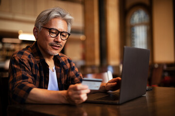 Fototapeta na wymiar Businessman working on laptop and sitting in cafe. Senior man holding credit card.