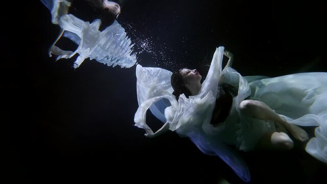 a drowning woman underwater, swimming and diving under the surface of a dark pool