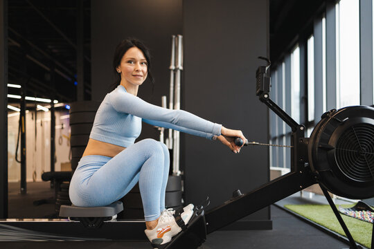 Side view of sports woman doing exercise on rowing machine