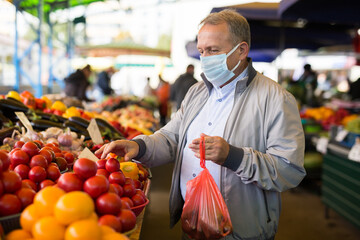 Man in face mask choosing tomatoes in greengrocery