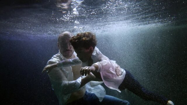 Father and his little son underwater, swimming and diving under the surface of a dark pool