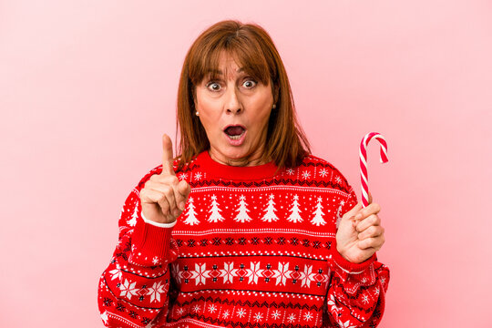 Middle age caucasian woman holding Christmas stick isolated on pink background having an idea, inspiration concept.