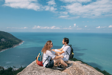 A couple stand on a rock at a viewpoint with an epic view of the ocean