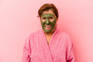 Middle age caucasian woman wearing a facial mask isolated on pink background screaming very angry and aggressive.