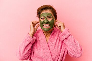 Middle age caucasian woman wearing a facial mask isolated on pink background covering ears with hands.