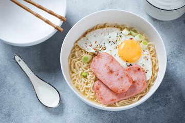 White bowl with Hong Kong breakfast or Gong Zai Mein, elevated view on a light-blue stone background