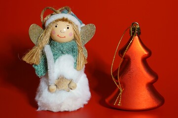 A toy Christmas angel and a Christmas tree close-up on a red background. New Year decorations.