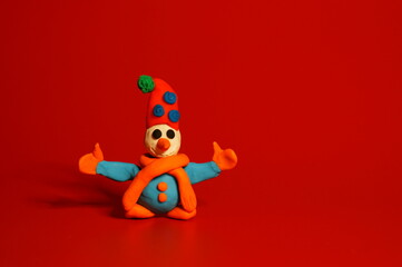 A toy snowman made of plasticine on a red background. Holiday photo.