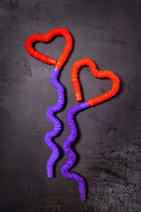 Tube toys bent as two red heart balloons and wavy ribbons on black