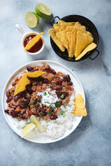 White plate with tex-mex chili con carne, nachos and dip sauce, top view over light-blue stone background, vertical shot