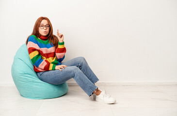 Fototapeta premium Young caucasian woman sitting on puff isolated on white background having some great idea, concept of creativity.