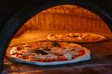 Due pizze Margherita napoletane con pomodoro, mozzarella di bufala e basilico fresco in cottura nel forno a legna 