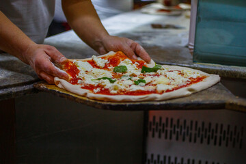 Pizzaiolo mentre adagia su una pala di legno una pizza margherita napoletana con pomodoro, basilico...