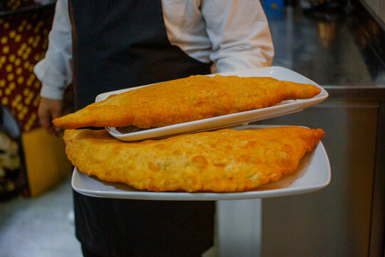 Cameriere di una pizzeria che porta due pizze fritte enormi ripiene di ricotta e cicoli di maiale